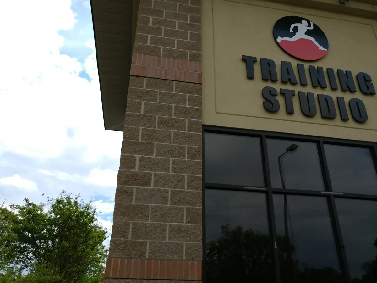 The Training Studio wordmark and runner badge on the tan brick of the Frankfort Avenue building, shot from below.