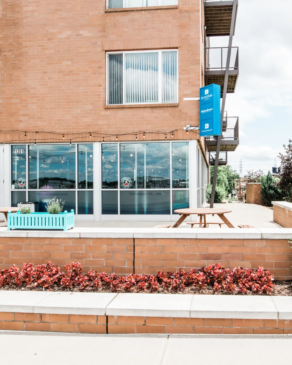 The Frankfort Avenue studio: a tan-brick building with a glass storefront, a picnic table and red flower beds out front.