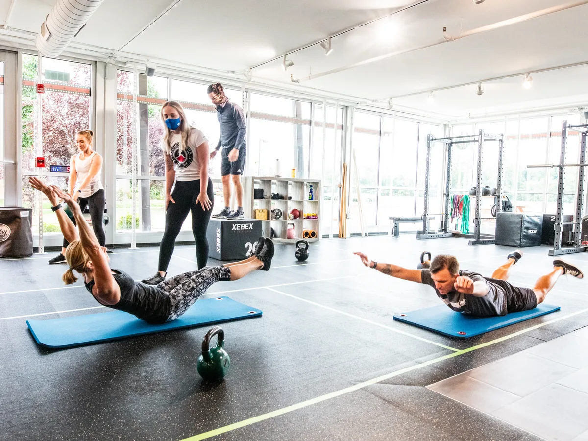 A small Get Fit & Stay Fit class holding floor positions on mats while two coaches spot, floor-to-ceiling windows behind.