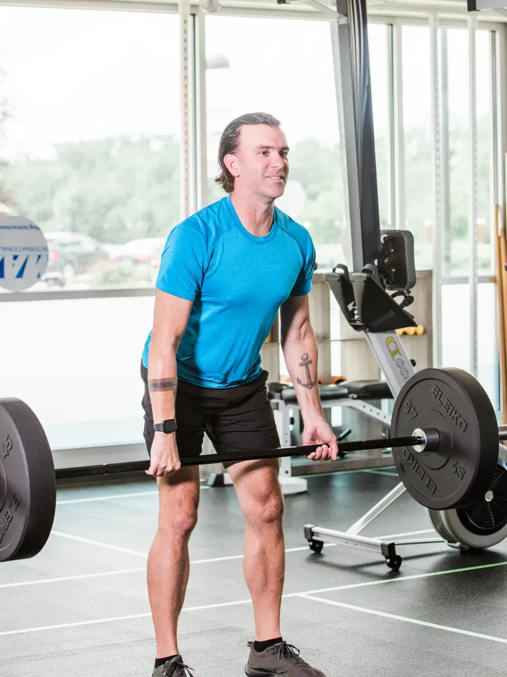 A member mid-deadlift with a loaded barbell in front of the studio windows.