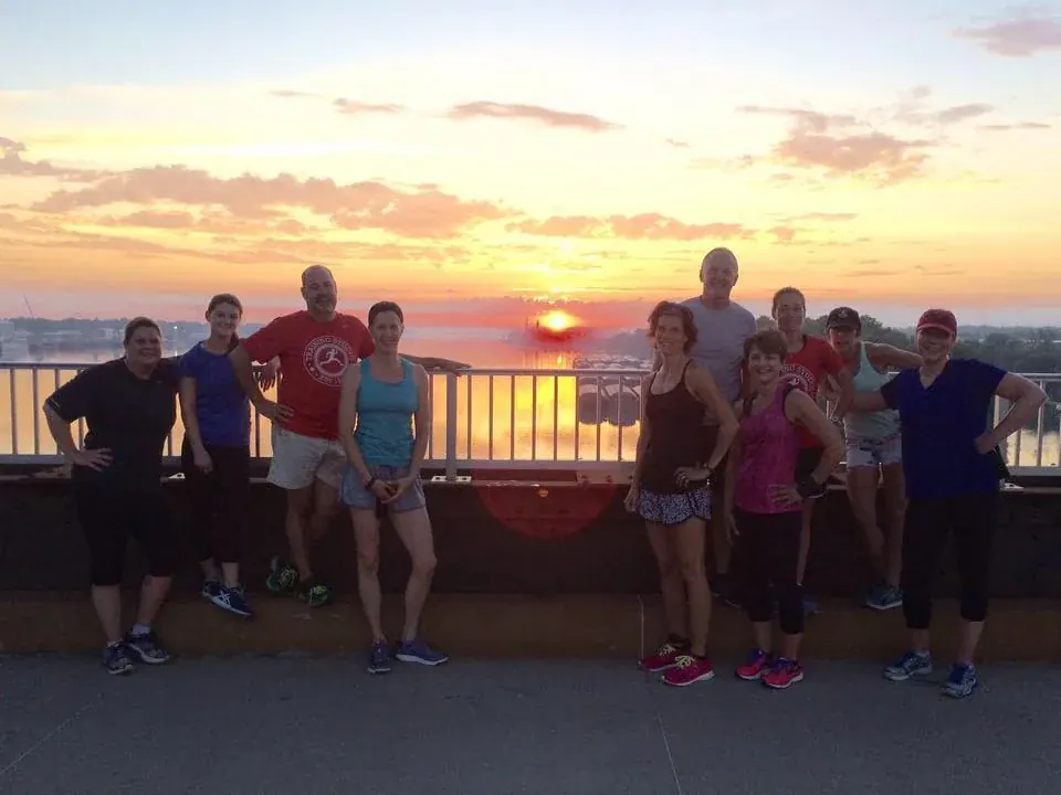The Running Club lined up along the riverfront railing at sunset after a Saturday run.